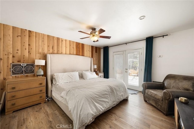 bedroom with access to exterior, ceiling fan, french doors, wood walls, and wood-type flooring