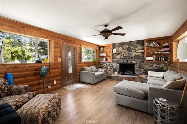 living room featuring ceiling fan, built in features, wood walls, hardwood / wood-style floors, and a fireplace