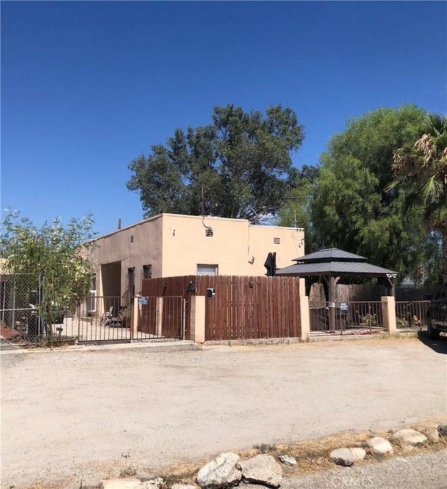 exterior space featuring stucco siding, a gazebo, a gate, and a fenced front yard