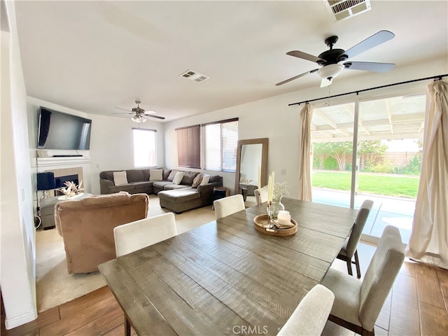 dining area featuring ceiling fan, light wood-type flooring, and a tiled fireplace