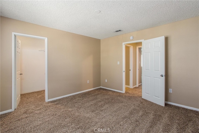 unfurnished bedroom featuring a textured ceiling, carpet, and a walk in closet