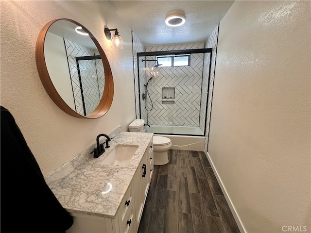 full bathroom with vanity, toilet, wood-type flooring, a textured ceiling, and combined bath / shower with glass door