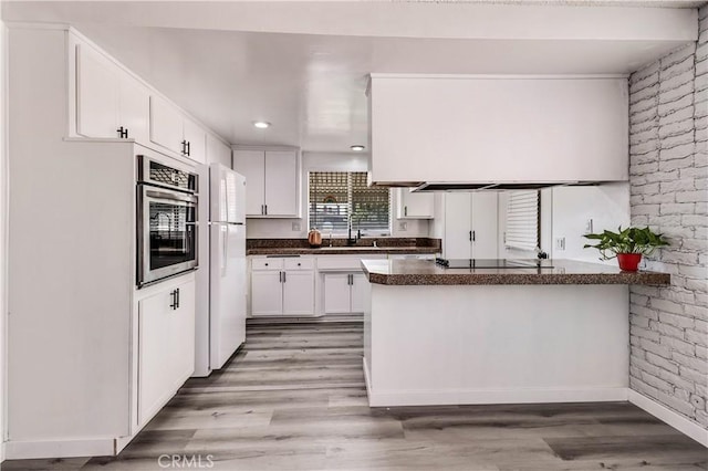 kitchen featuring stainless steel oven, kitchen peninsula, white fridge, and white cabinets