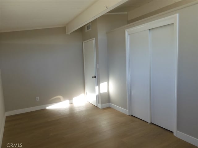 unfurnished bedroom with beamed ceiling, light hardwood / wood-style flooring, and a closet