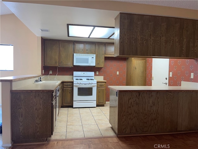 kitchen with light tile patterned flooring, white appliances, kitchen peninsula, dark brown cabinetry, and sink