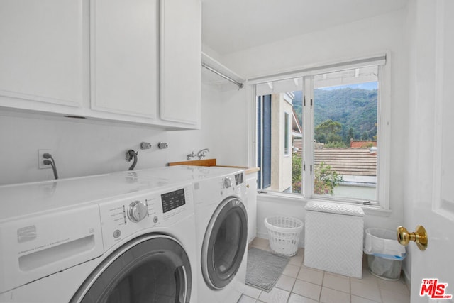 clothes washing area featuring cabinets, light tile patterned floors, and washer and clothes dryer