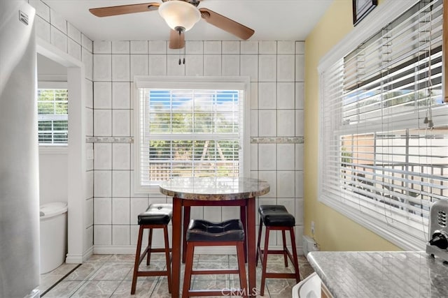 dining room featuring ceiling fan, tile walls, and a healthy amount of sunlight