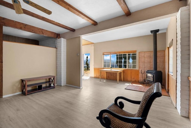 sitting room with a wood stove, light hardwood / wood-style floors, and beamed ceiling