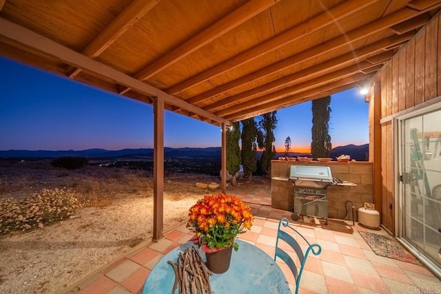 patio terrace at dusk featuring exterior kitchen, a mountain view, and area for grilling