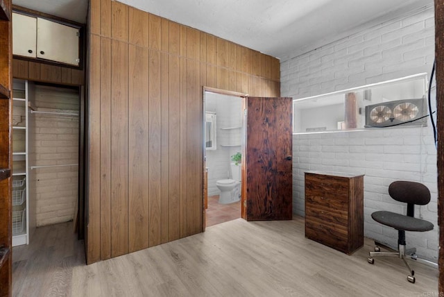 bedroom featuring brick wall, light wood-type flooring, connected bathroom, and wood walls