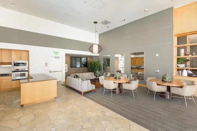 kitchen with appliances with stainless steel finishes, hanging light fixtures, a towering ceiling, and light brown cabinets