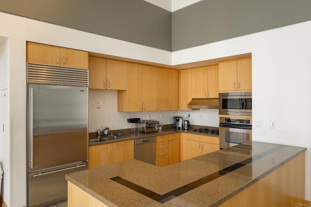 kitchen with light brown cabinets, sink, kitchen peninsula, built in appliances, and a towering ceiling