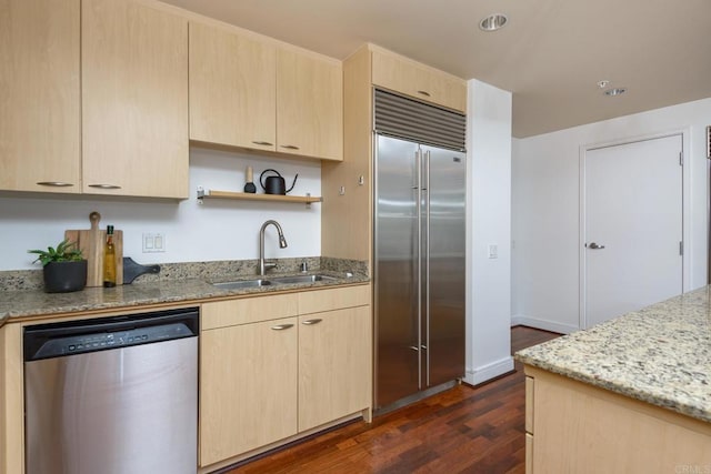 kitchen featuring appliances with stainless steel finishes, light stone countertops, light brown cabinets, dark hardwood / wood-style flooring, and sink