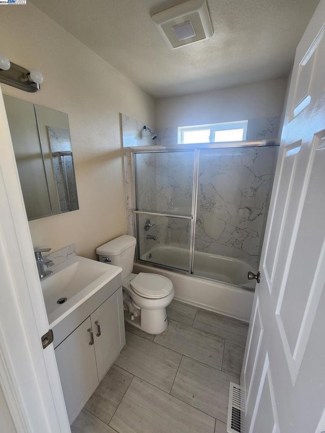 full bathroom featuring enclosed tub / shower combo, a textured ceiling, vanity, and toilet