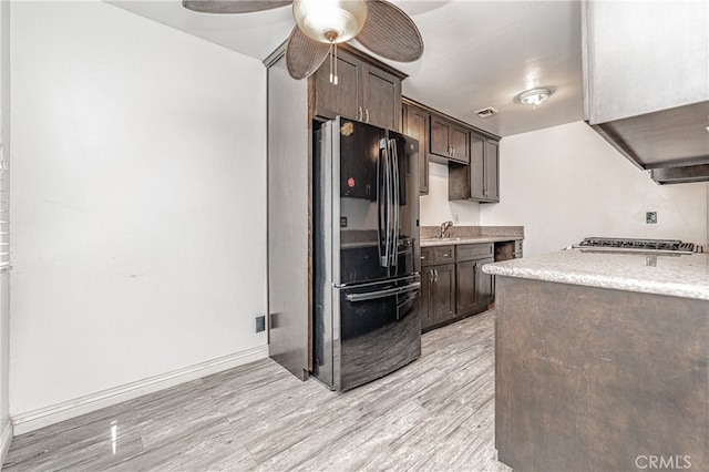 kitchen featuring light hardwood / wood-style flooring, dark brown cabinets, stainless steel gas cooktop, and black fridge