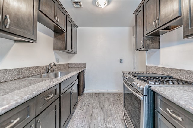 kitchen featuring light hardwood / wood-style flooring, dark brown cabinets, stainless steel gas range oven, and sink