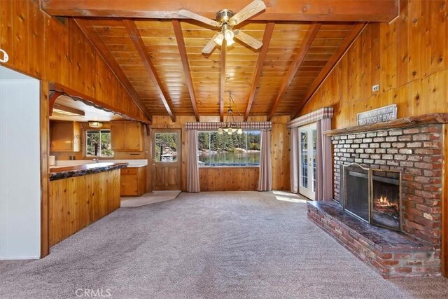 unfurnished living room with a brick fireplace, wooden ceiling, carpet flooring, and wooden walls