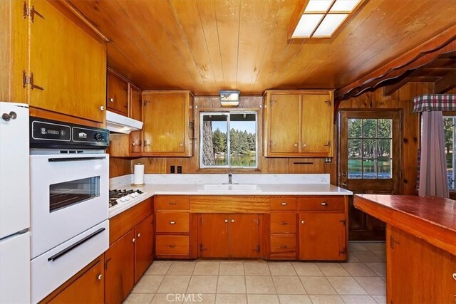 kitchen with light tile patterned flooring, sink, wood walls, white appliances, and wooden ceiling