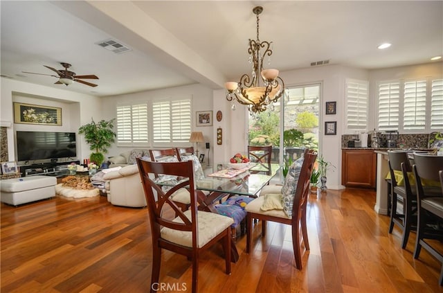 dining area with ceiling fan with notable chandelier, wood-type flooring, and a healthy amount of sunlight