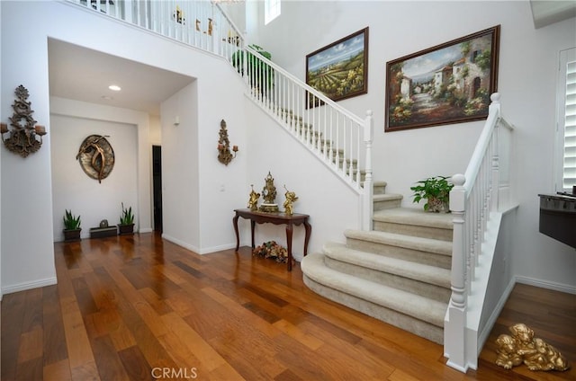 staircase featuring a towering ceiling and wood-type flooring