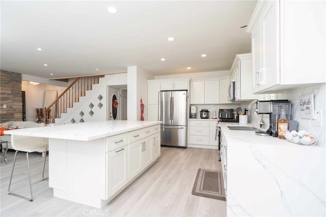 kitchen featuring white cabinetry, sink, light stone counters, decorative backsplash, and appliances with stainless steel finishes