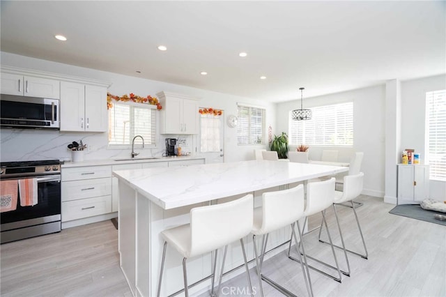 kitchen featuring sink, stainless steel appliances, a kitchen island, tasteful backsplash, and white cabinets