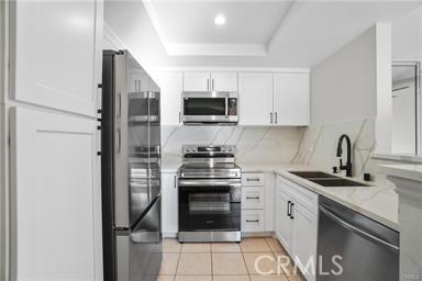 kitchen featuring light stone counters, stainless steel appliances, a tray ceiling, sink, and white cabinets