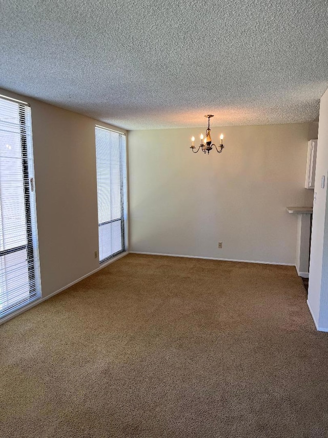 empty room with a textured ceiling, carpet flooring, and a chandelier