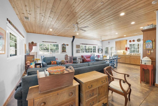 living room with wooden ceiling, ceiling fan, a wood stove, and a wealth of natural light