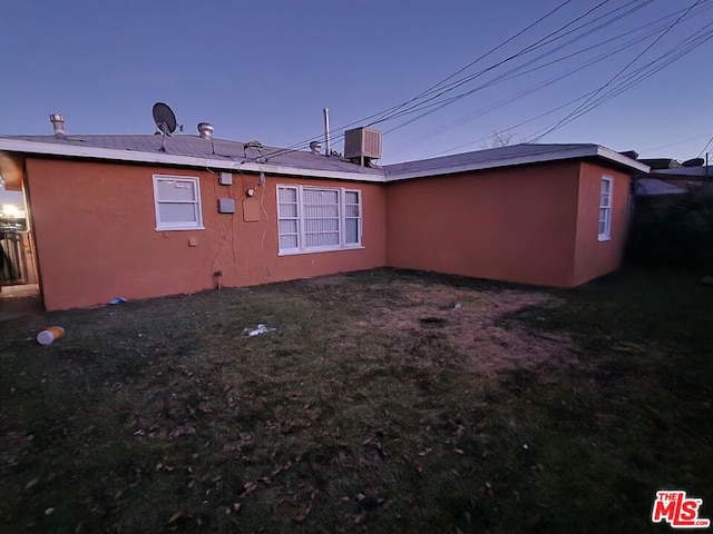 back house at dusk with a lawn and central AC