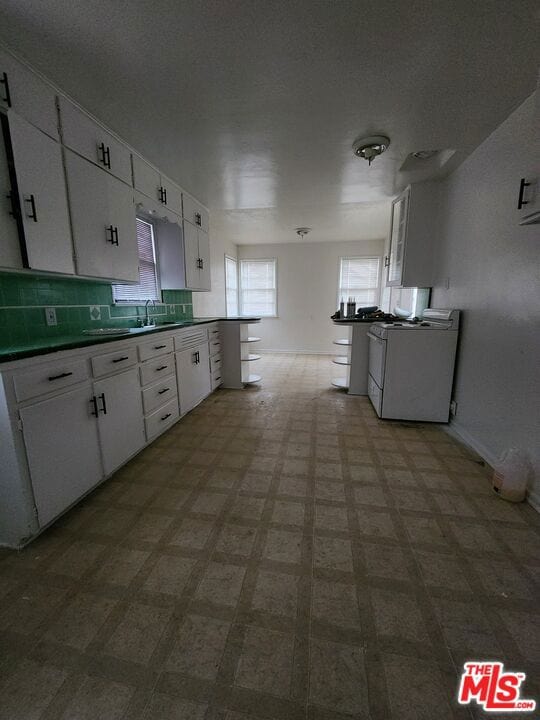 kitchen with sink, kitchen peninsula, tasteful backsplash, white gas range oven, and white cabinetry