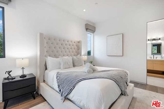 bedroom featuring light hardwood / wood-style floors, ensuite bath, and sink