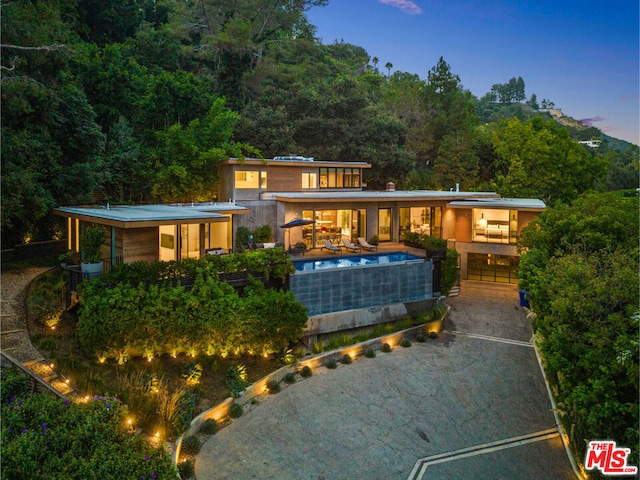 back house at dusk with a balcony and a pool