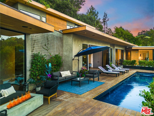 pool at dusk with an outdoor hangout area and a deck