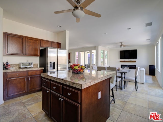 kitchen featuring ceiling fan, stainless steel fridge with ice dispenser, a kitchen breakfast bar, a center island, and light stone countertops