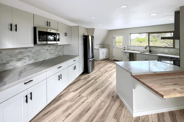 kitchen with wooden counters, white cabinets, sink, light wood-type flooring, and appliances with stainless steel finishes