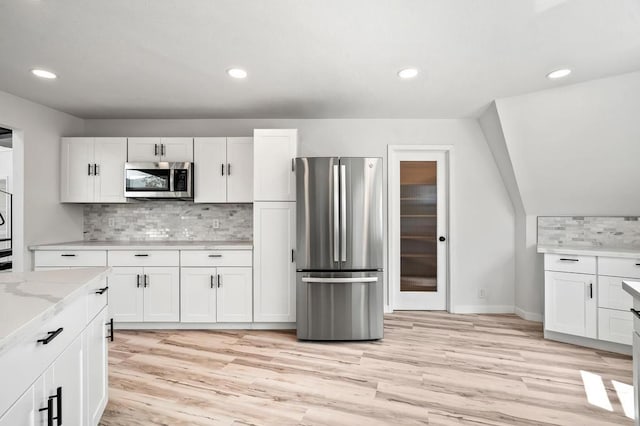 kitchen with light hardwood / wood-style floors, light stone counters, white cabinetry, and appliances with stainless steel finishes