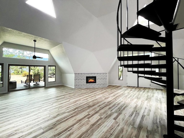 unfurnished living room featuring a tiled fireplace, ceiling fan, wood-type flooring, and lofted ceiling