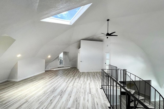 additional living space with a textured ceiling, light hardwood / wood-style floors, ceiling fan, and vaulted ceiling with skylight