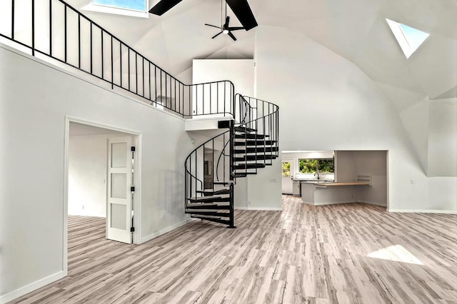 stairway featuring wood-type flooring, a skylight, high vaulted ceiling, and ceiling fan