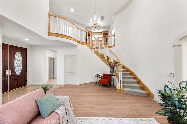 entrance foyer featuring a towering ceiling, an inviting chandelier, light hardwood / wood-style flooring, and crown molding