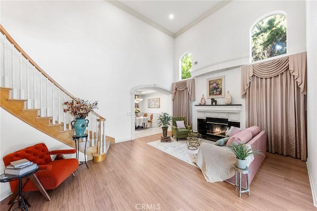 living room featuring a tile fireplace, a towering ceiling, light hardwood / wood-style floors, and ornamental molding