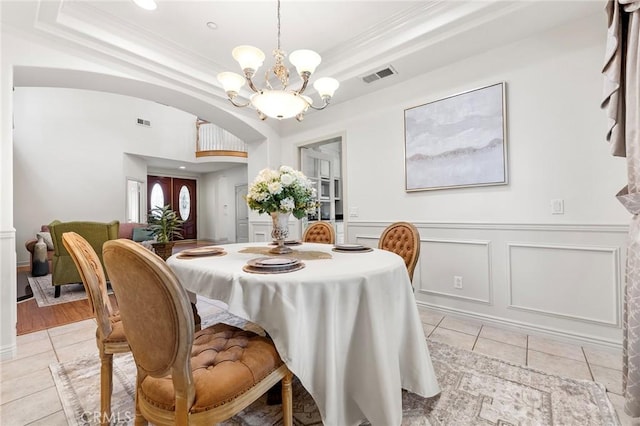 dining space with light tile patterned flooring, a raised ceiling, ornamental molding, and an inviting chandelier