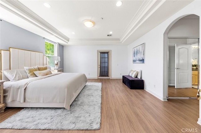 bedroom with light hardwood / wood-style floors, a raised ceiling, and crown molding