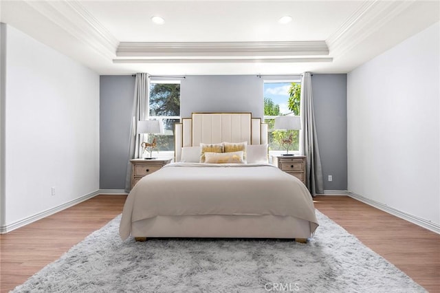 bedroom with a raised ceiling, multiple windows, ornamental molding, and light wood-type flooring