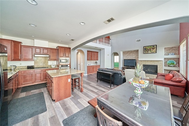 kitchen with appliances with stainless steel finishes, a kitchen breakfast bar, light hardwood / wood-style floors, light stone counters, and a center island