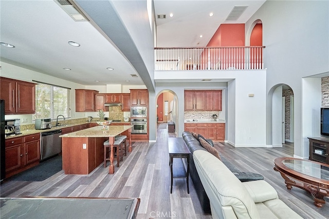 kitchen with a kitchen island, a kitchen breakfast bar, stainless steel appliances, high vaulted ceiling, and hardwood / wood-style floors