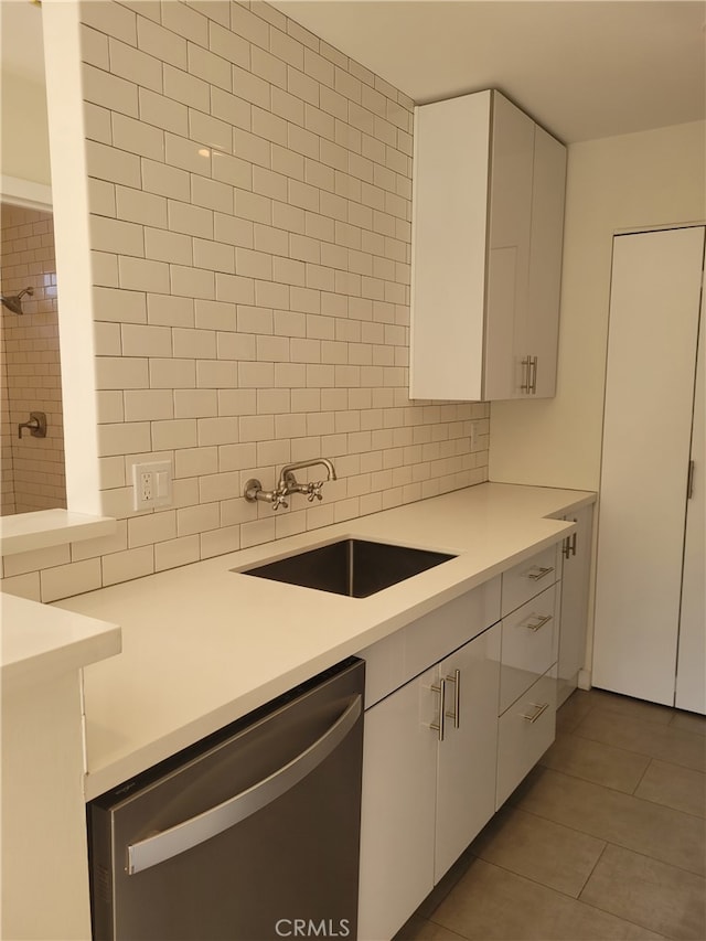 kitchen with dark tile patterned floors, dishwasher, tasteful backsplash, sink, and white cabinetry