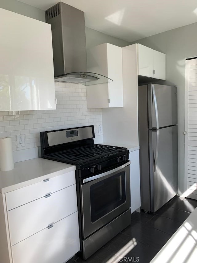 kitchen with appliances with stainless steel finishes, wall chimney exhaust hood, tasteful backsplash, and white cabinetry