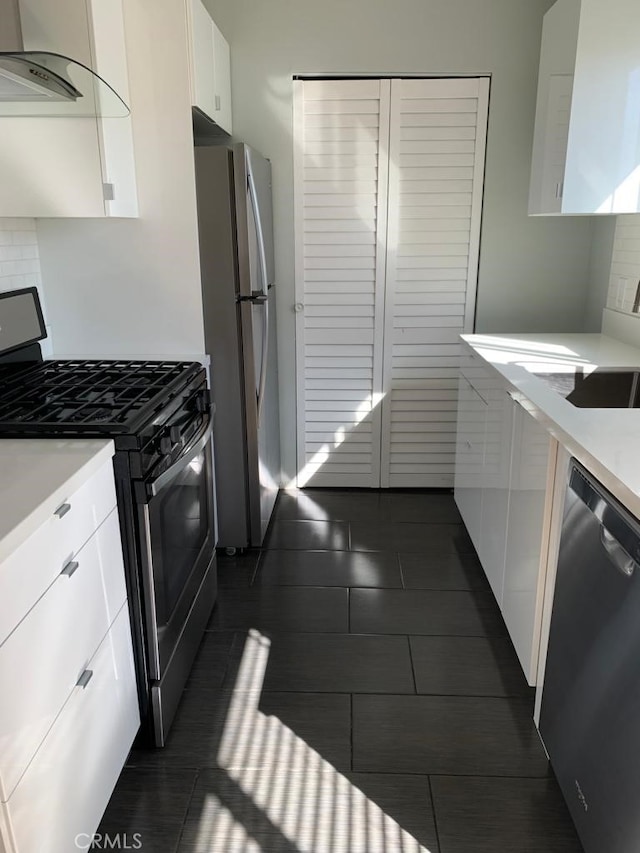 kitchen with white cabinets, dark tile patterned flooring, backsplash, appliances with stainless steel finishes, and range hood